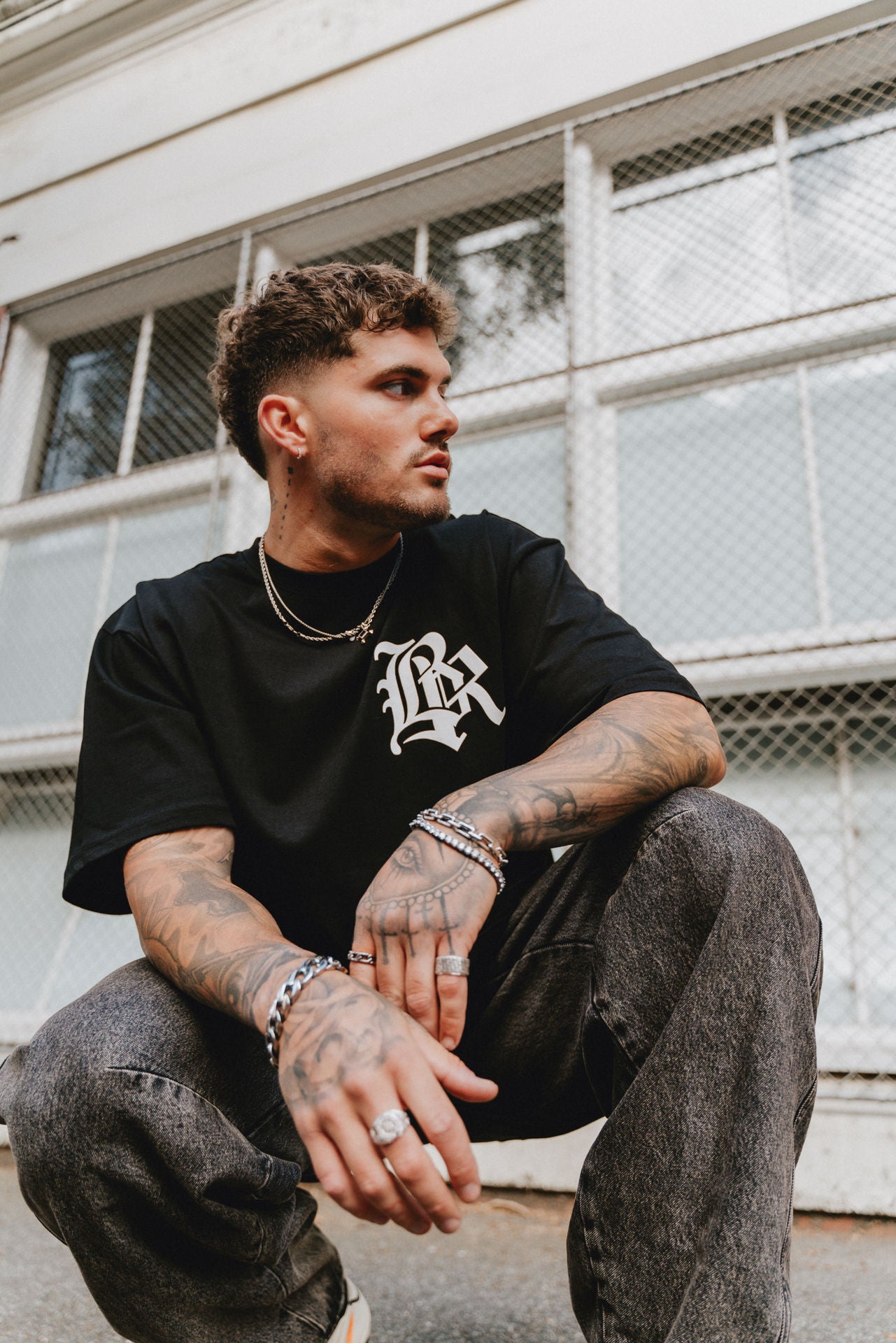 male model crouching, wearing a black t-shirt in an urban setting