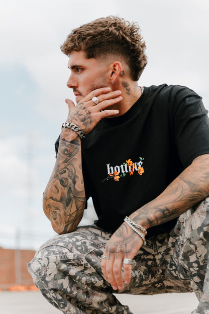 male model crouching in urban setting wearing a flower streetwear t-shirt, and cargo pants