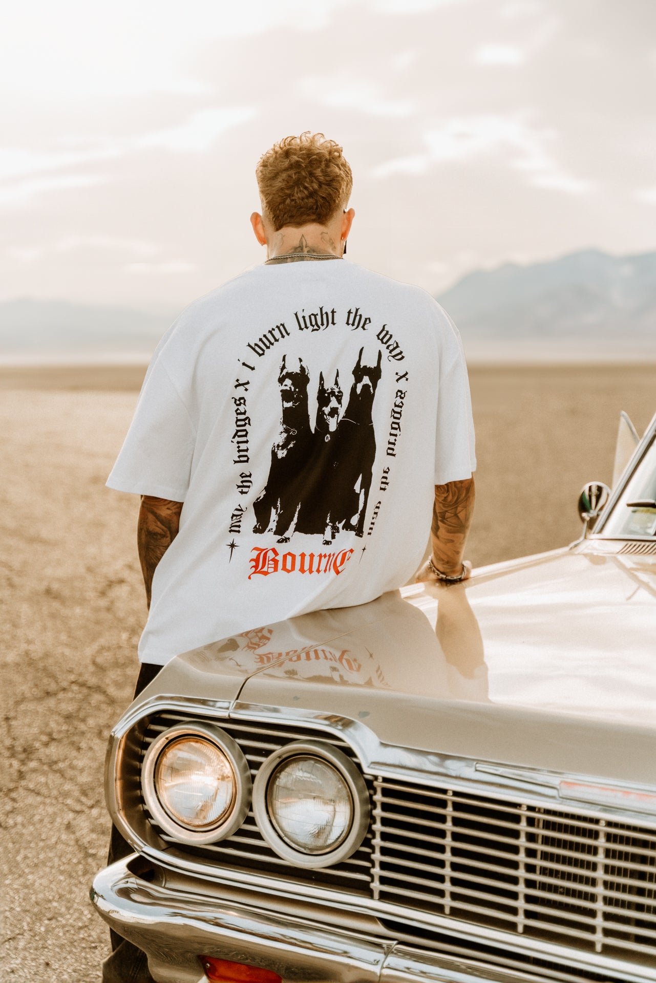 male model leaning on a car, wearing white t-shirt with doberman dogs on it