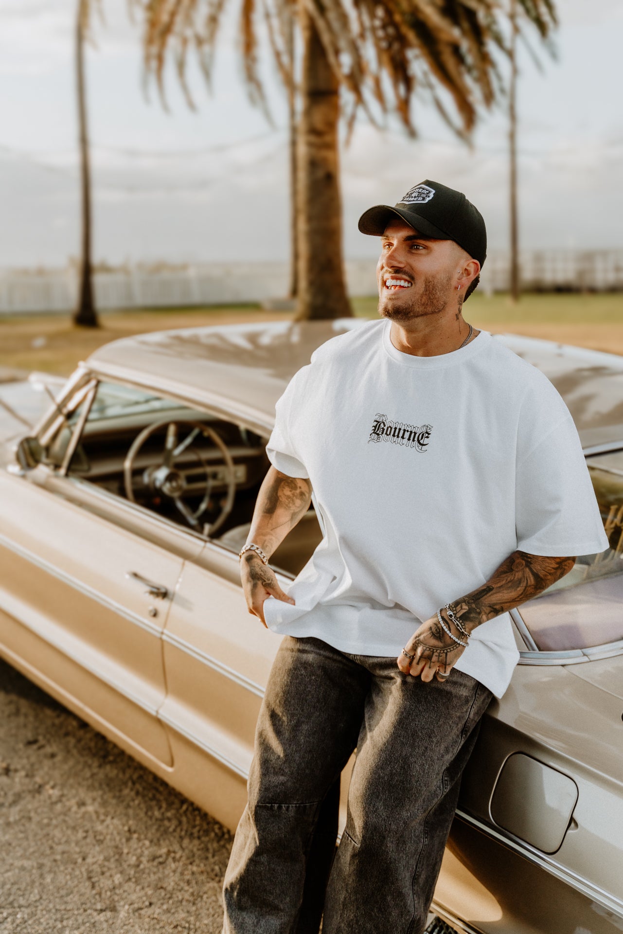 male model smiling leaning against a car