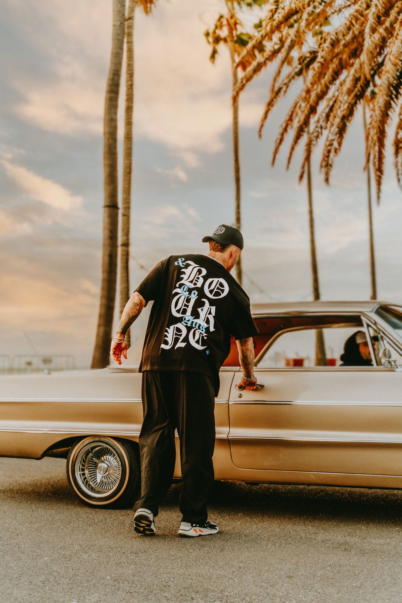 Male model wearing black, white and blue streetwear tee, beach setting, palm trees