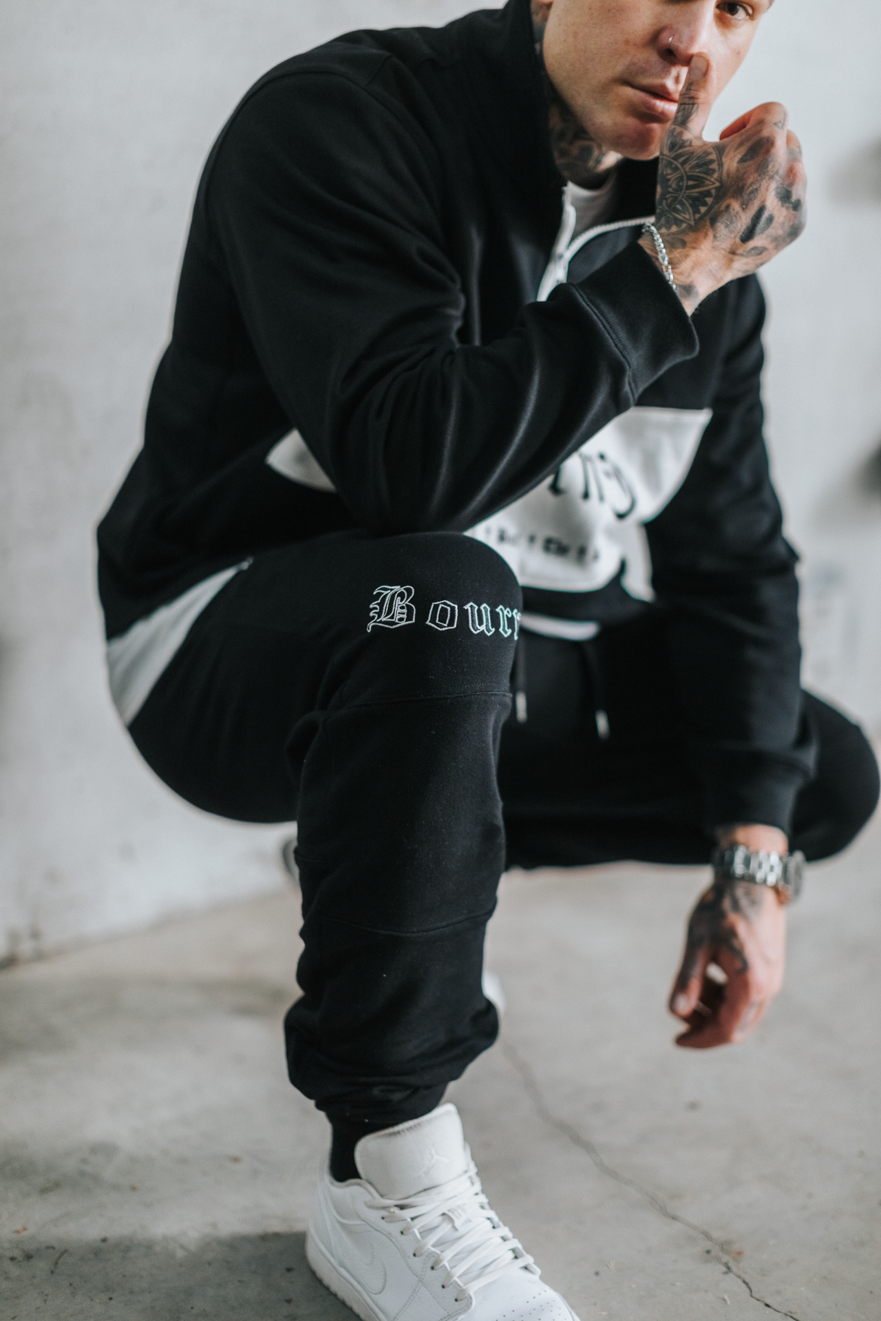 male model kneeling down, wearing black and white tracksuit in an urban setting