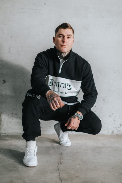 male model kneeling down, wearing black and white tracksuit in an urban setting