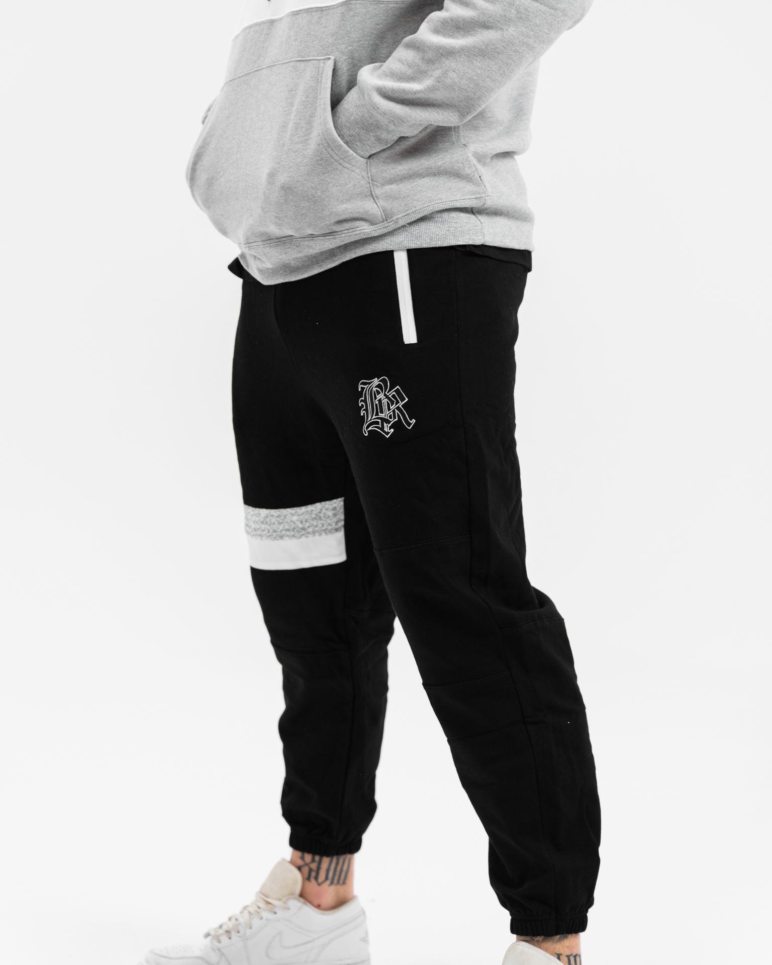 male model with white and grey hoodie and black tracksuit pants, white background