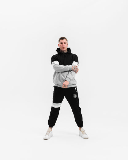 male model with black, white and grey hoodie and black tracksuit pants, white background