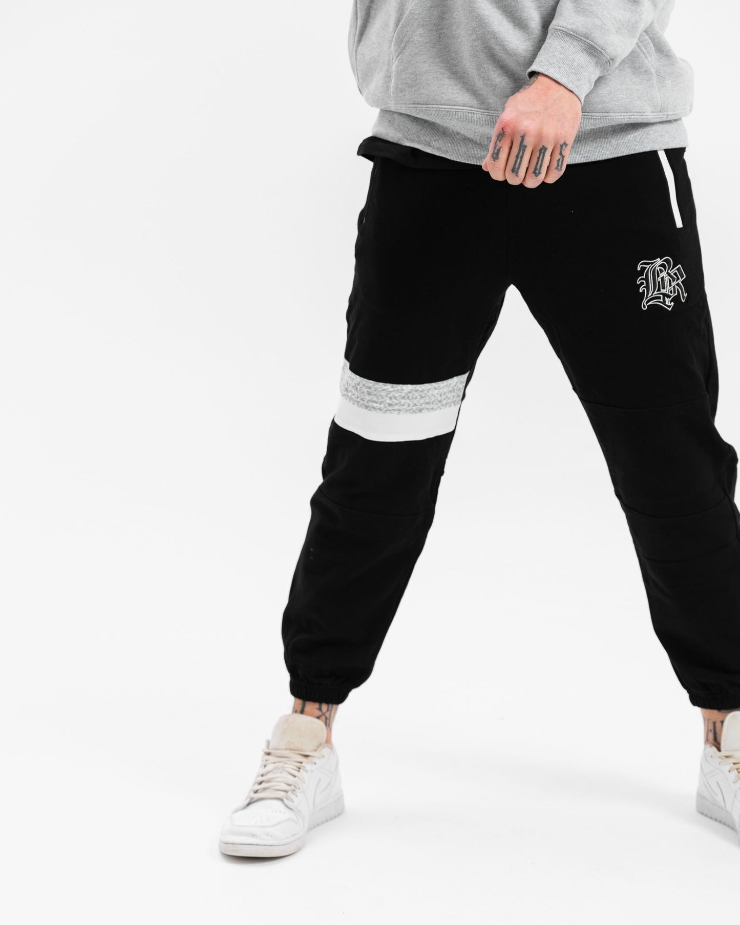 male model with white and grey hoodie and black tracksuit pants, white background