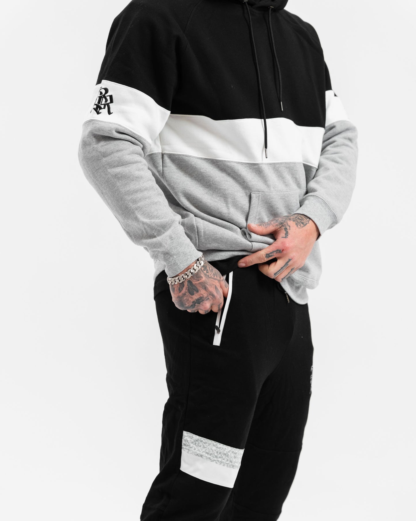 male model with black, white and grey hoodie and black tracksuit pants, white background