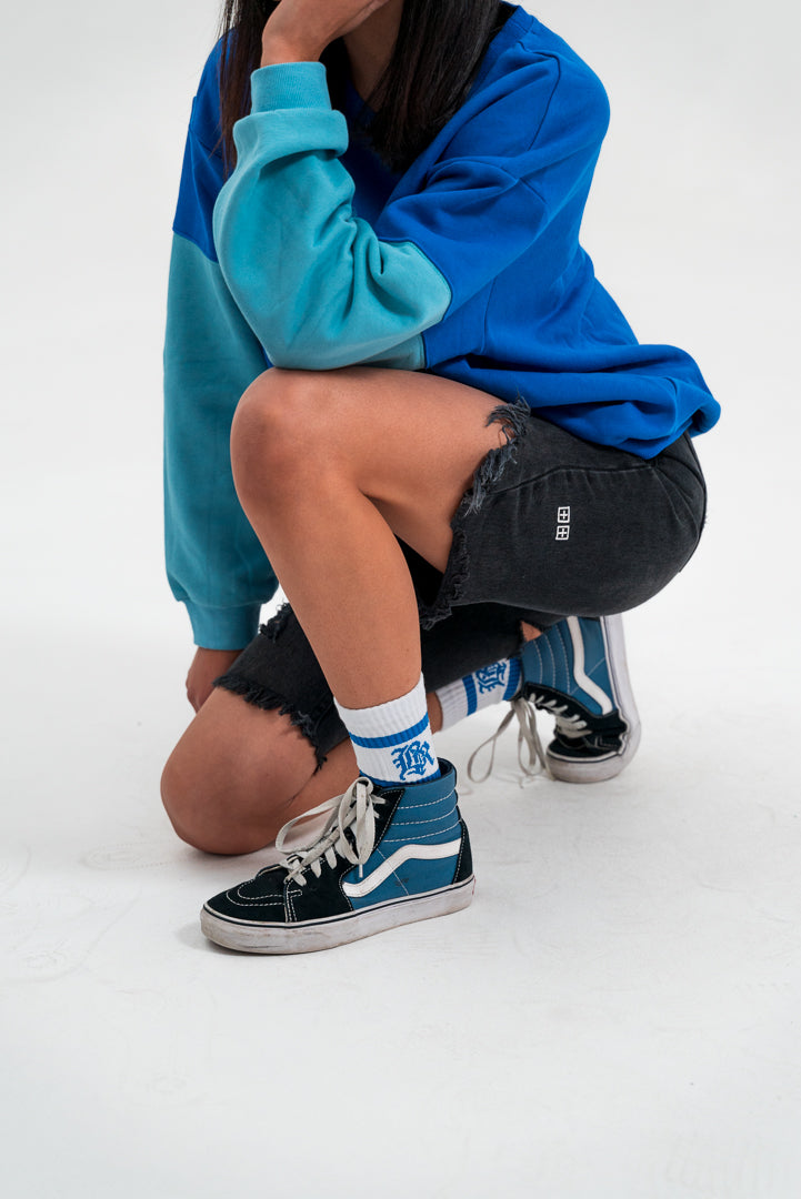 female model looking away, wearing a blue and teal crewneck hoodie and black bottoms, white background