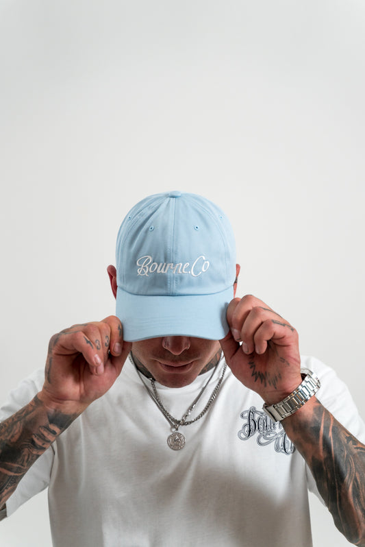 male model wearing a blue hat, tattoos, chains, watch, white background