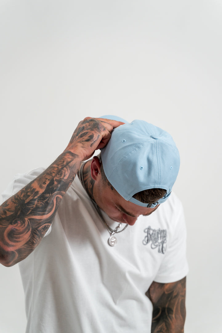 male model wearing a blue hat, tattoos, chains, watch, white background