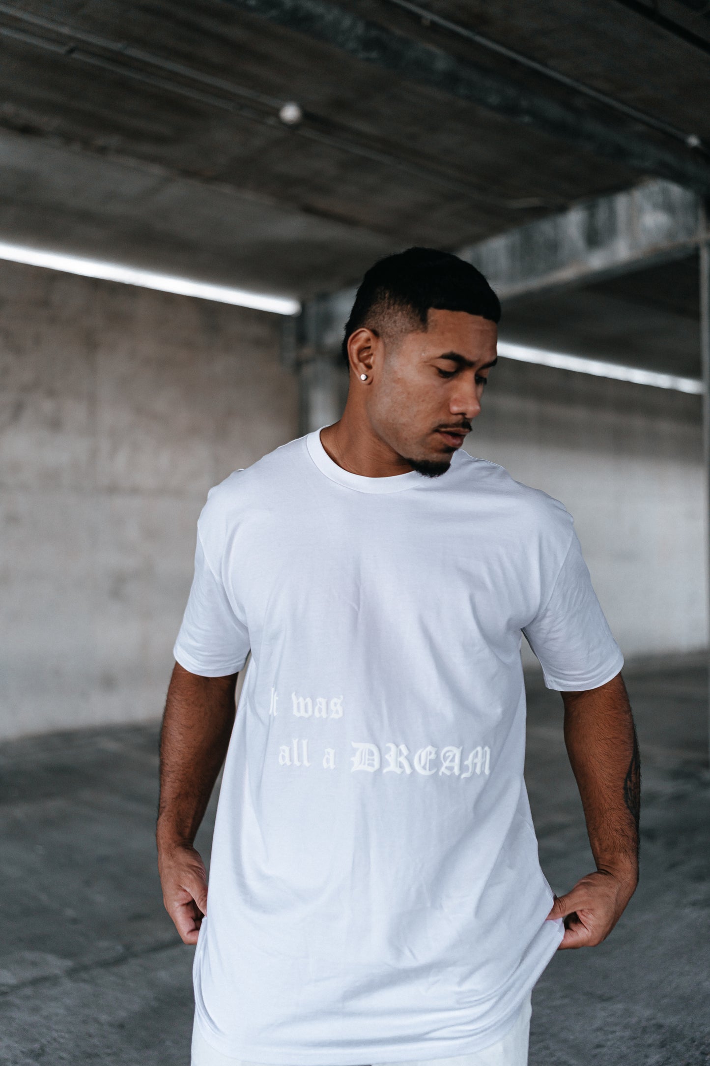 male model looking down, with a white t-shirt on, urban setting