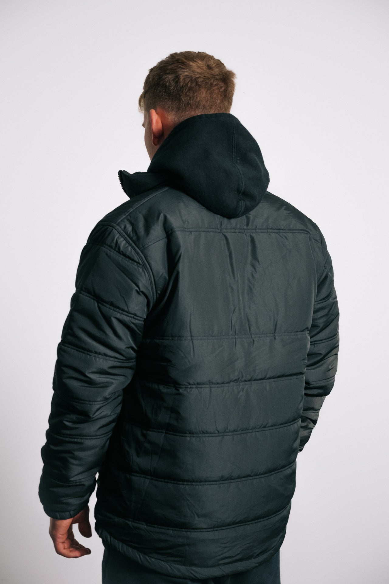 male model facing away, wearing black puffer jacker, white background